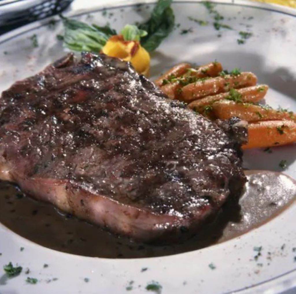 A steak with a dark sauce, accompanied by a side of carrots and a small garnish.