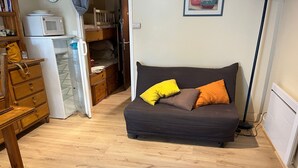 Ett kompakt bostadsutrymme med en soffa, ett träskommod och en liten köksdel som inkluderar en mikrovågsugn och ett kylskåp.
