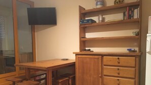 Ett skrivbord i trä med en tv som är monterad på väggen, en bokhylla med böcker och dekorativa föremål samt ett träskåp med lådor.