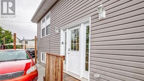 Une maison à deux étages avec un porche à l’avant, une voiture rouge garée dans l’allée et une boîte aux lettres sur la porte d’entrée.