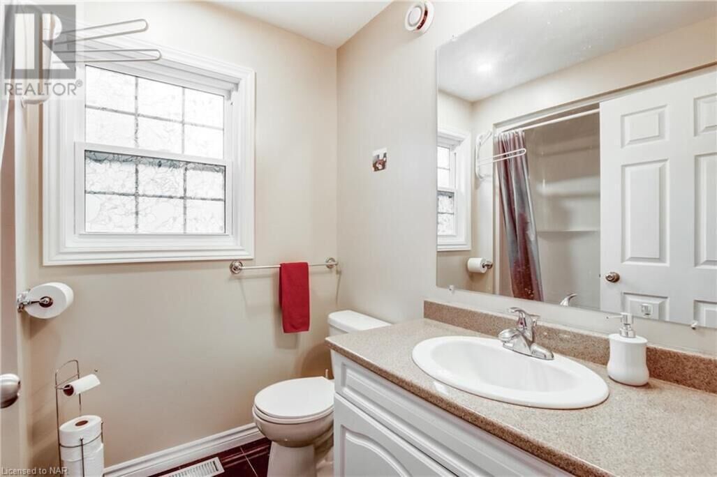 A bathroom with a white toilet, a sink, a mirror, and a window with a towel hanging on the wall.