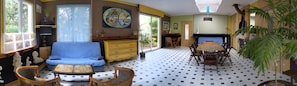 Une pièce comprenant un canapé, des fauteuils, une table à manger, une cheminée et une grande fenêtre.