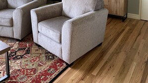 Una sala de estar con dos sillones grises, un aparador de madera, un televisor y un reloj en la pared.