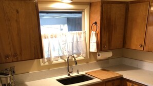 Una cocina compacta con armarios de madera, lavavajillas integrado, pileta y ventana con cortinas.