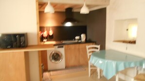 Een compacte keuken met een wasmachine, een eettafel met stoelen en hanglampen.
