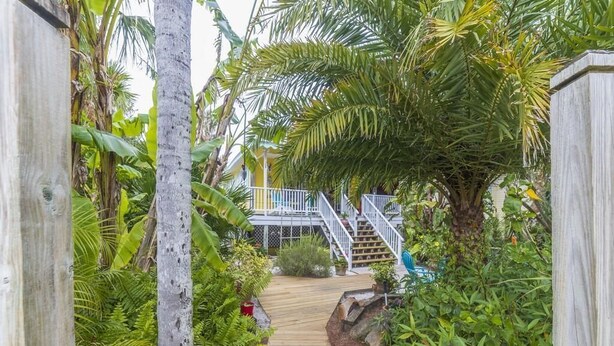 A wooden pathway leading to a house with a white railing staircase.