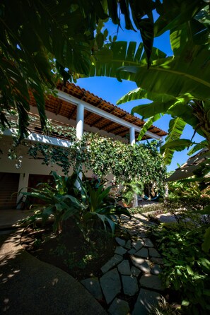 A building with a stone pathway, lush greenery, and a clear blue sky.