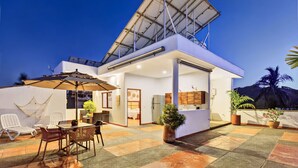 A modern house with a flat roof, a balcony, and a dining area with chairs and a table.