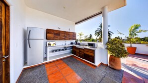 A modern kitchen with a refrigerator, wooden cabinets, and a large window overlooking a garden.