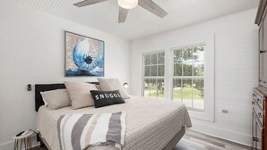 A bedroom with a bed, a ceiling fan, a window with blinds, and a painting on the wall.