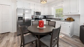 A modern kitchen with white cabinets, stainless steel appliances, and a dining area with a round table and chairs.