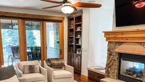 Un salon avec une cheminée, un ventilateur de plafond et un téléviseur fixé au mur.
