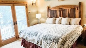 Une chambre à coucher avec un grand lit, un ventilateur de plafond, une tête de lit en bois et une porte-fenêtre coulissante.