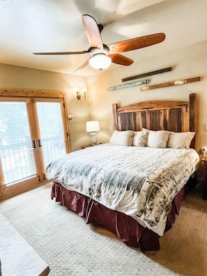 Un dormitorio con una cama grande, un ventilador de techo, cabecera de madera y una puerta corrediza de vidrio.