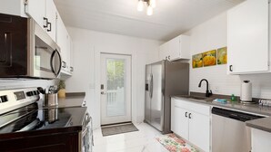 A modern kitchen with white cabinetry, stainless steel appliances, and a tiled floor. - Beach Cottage with 2 king beds-One short block to beach-Walk to Pier Village! (St. Simons Island)