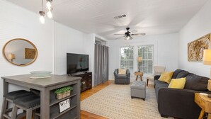 A modern living room with a TV, sofa, and dining area. - Beach Cottage with 2 king beds-One short block to beach-Walk to Pier Village! (St. Simons Island)
