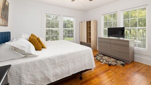 A bedroom with a bed, a dresser, a television, and large windows. - Beach Cottage with 2 king beds-One short block to beach-Walk to Pier Village! (St. Simons Island)