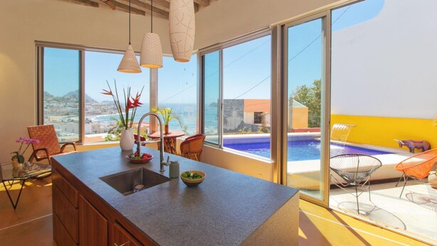 Eine moderne Küche mit einer großen Kochinsel, großen Fenstern und Blick auf Pool und Meer.