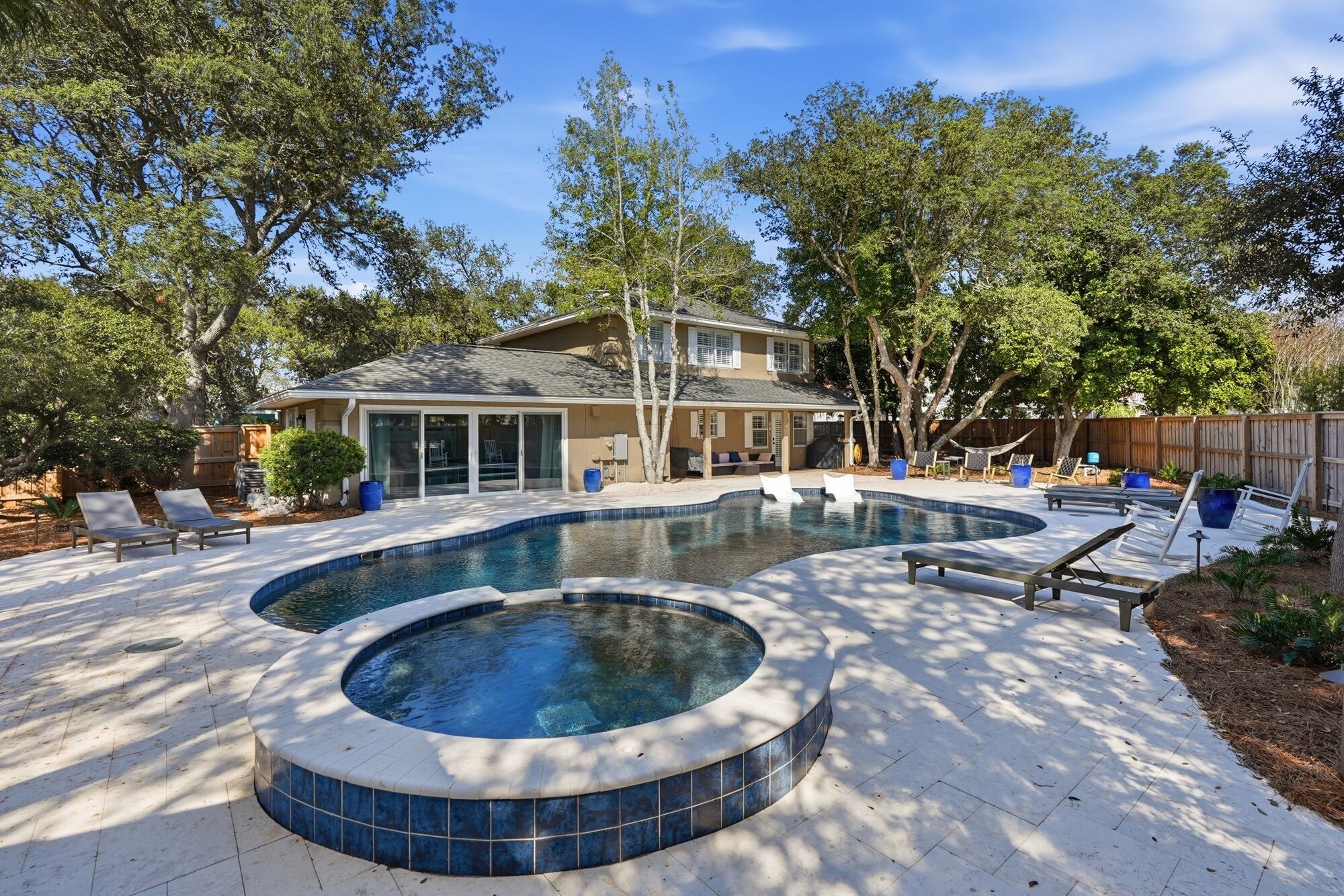 A backyard with a swimming pool, lounge chairs, and a covered patio area.