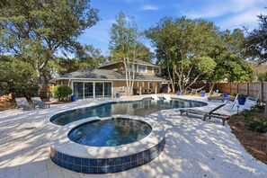 A backyard with a swimming pool, lounge chairs, and a covered patio area.