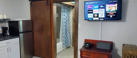 A modern kitchen with a refrigerator, a wooden cabinet, and a television mounted on the wall displaying various channels.