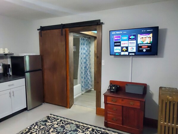 A modern kitchen with a refrigerator, a wooden cabinet, and a television mounted on the wall displaying various channels.
