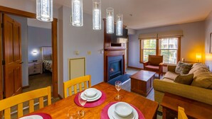 A dining area with a wooden table set for four, a fireplace, and a sofa in the background.