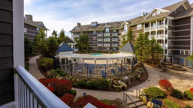 A resort with a central pool area surrounded by a fence, multiple buildings with balconies, and a well-maintained garden with various plants and trees.