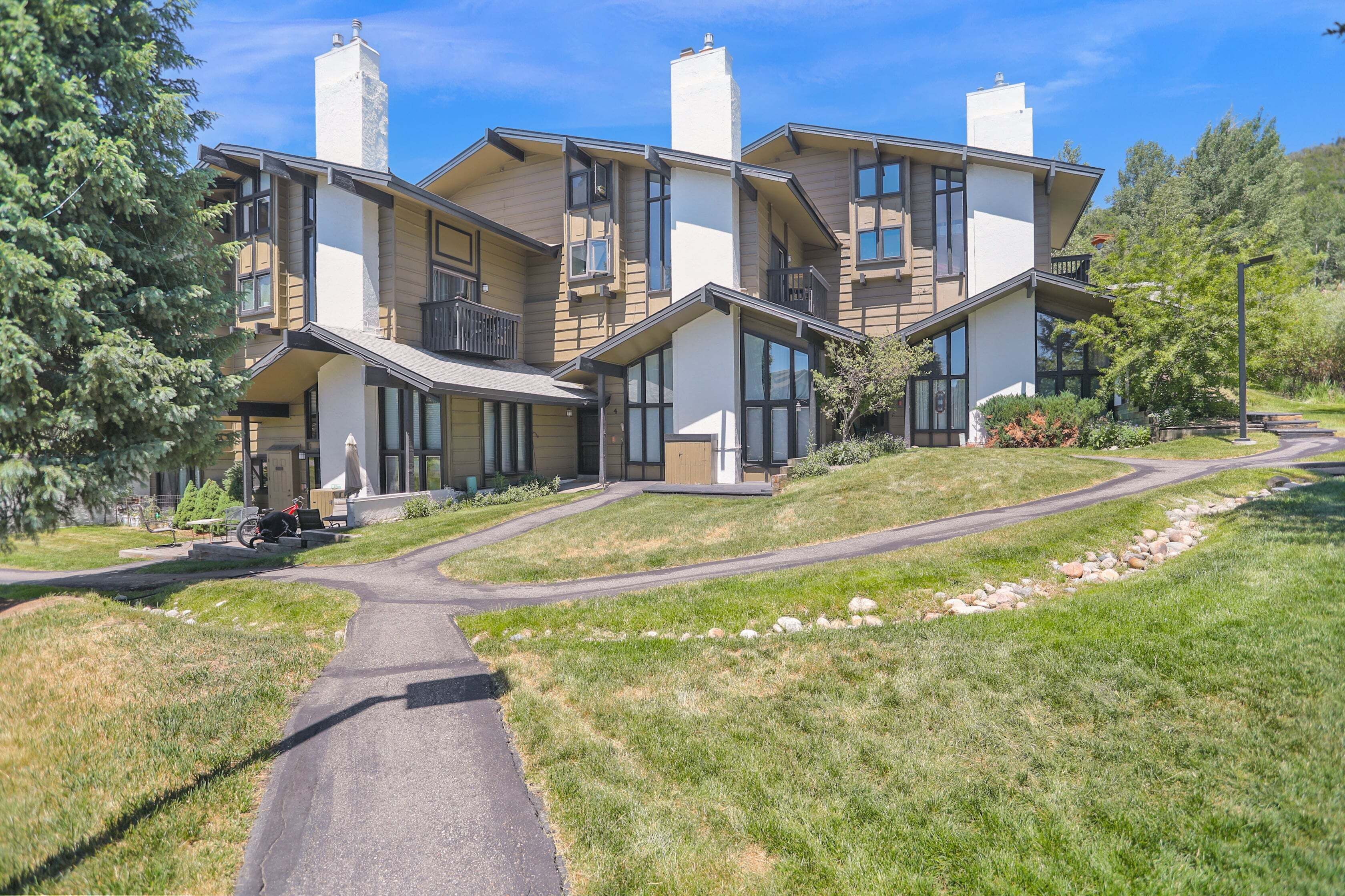 A modern multi-story building with a sloped roof, large windows, and a paved driveway leading to the entrance.