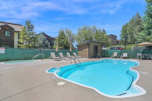 A swimming pool with lounge chairs, a small pool house, and a fenced area with trees.
