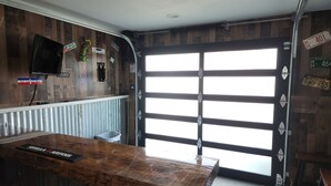 A bar area with a wooden counter, a television mounted on the wall, and various signs and decorations. - Beautiful Waterfront  Home on a Private Lake!   (Quinlan)