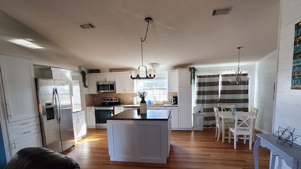 A spacious kitchen with a central island, white cabinetry, and a dining area with a striped curtain. - Beautiful Waterfront  Home on a Private Lake!   (Quinlan)