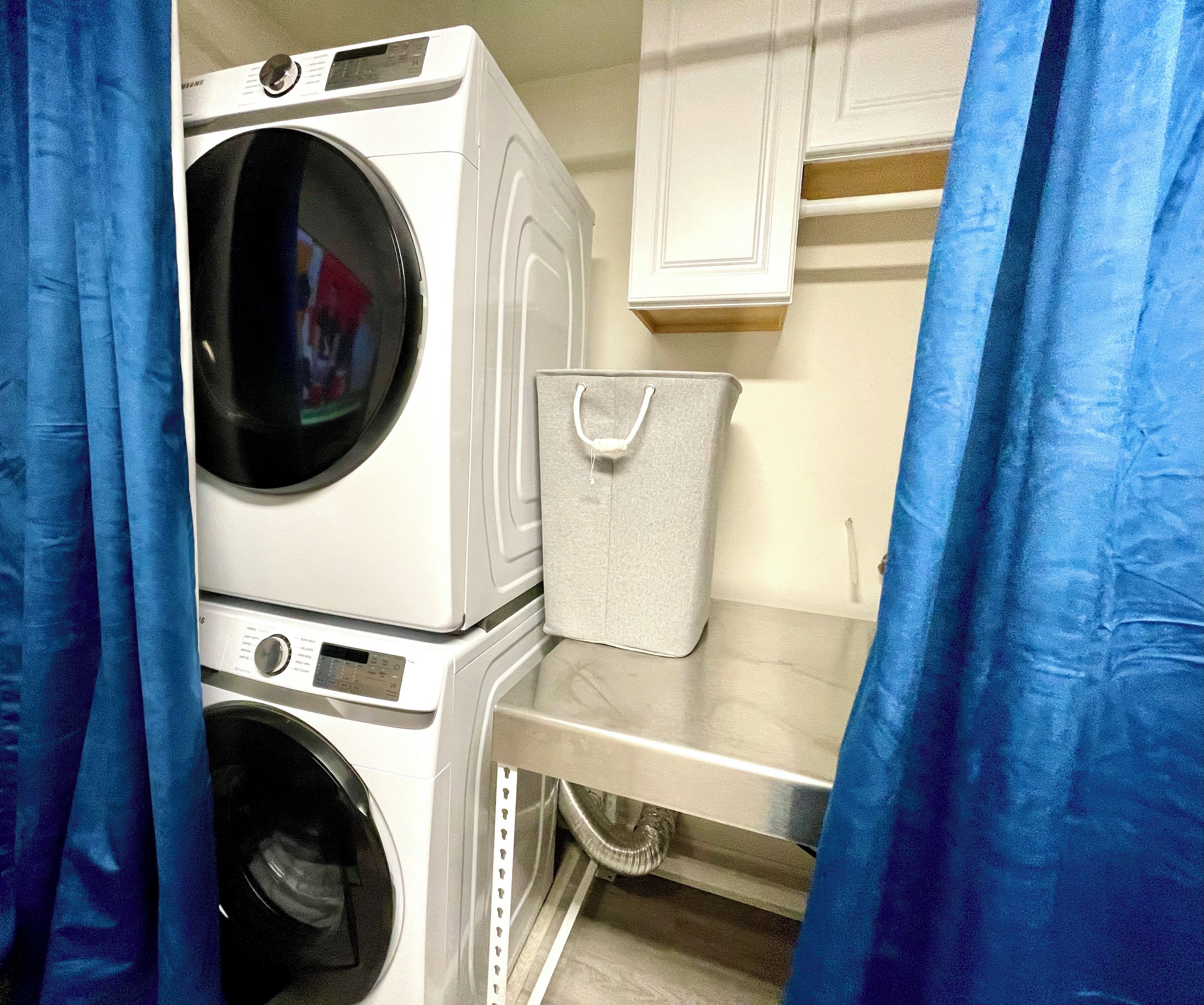 A laundry area with stacked washing machines, a drying rack, and a storage basket.