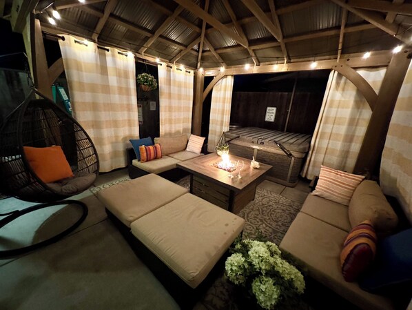 A cozy outdoor seating area with a cushioned sofa, a hanging chair, and a table with a candle.