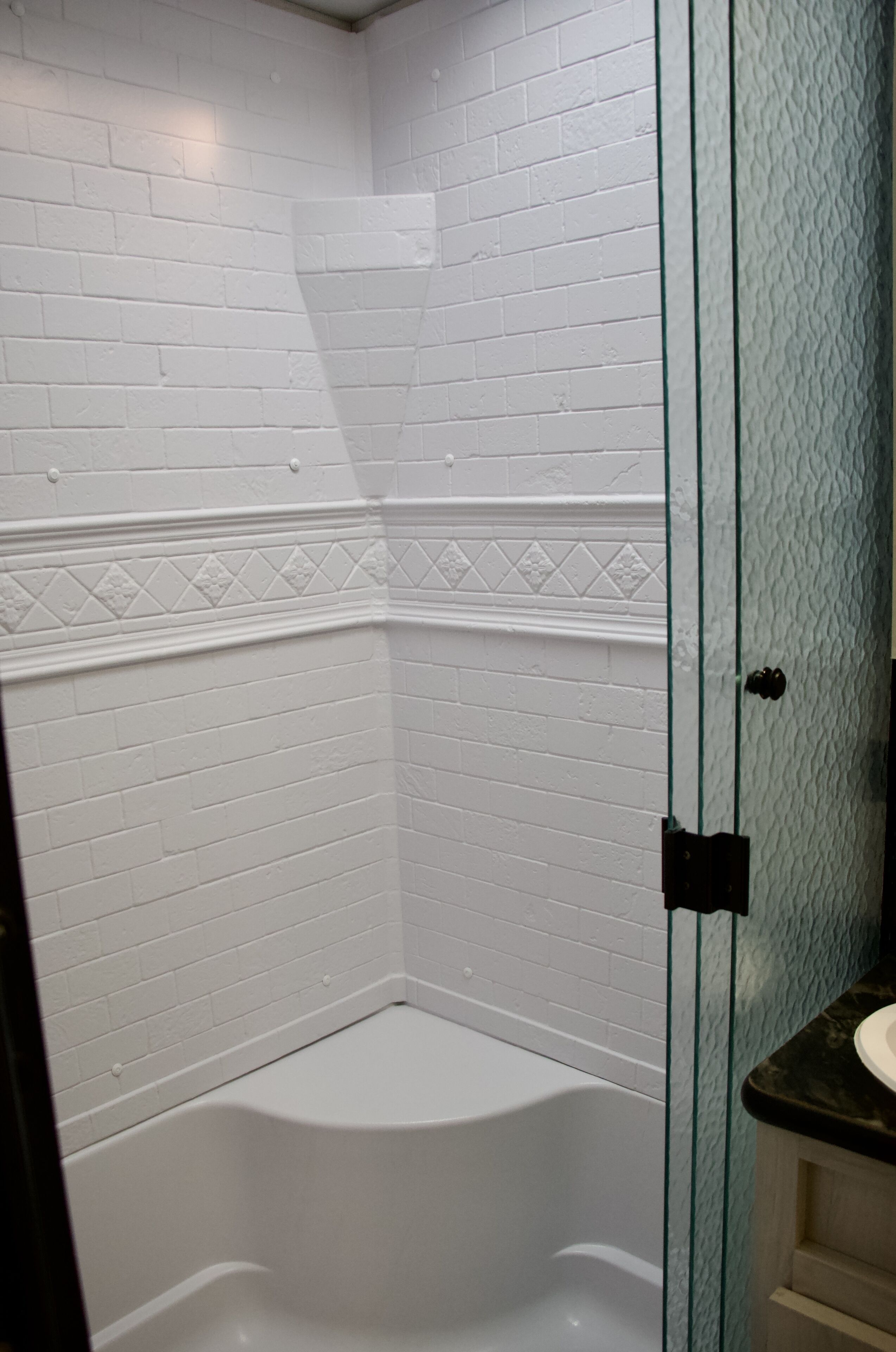 A corner bathroom with white brick walls, a white bathtub, and a glass shower enclosure.