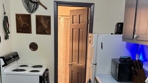 A compact kitchen with a stove, microwave, and cabinets. A wooden door leads to another room.