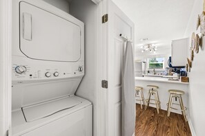 A modern kitchen with a built-in washer and dryer, wooden bar stools, and a view of the outdoors.