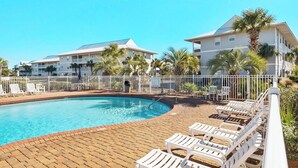A swimming pool with lounge chairs and a white fence.
