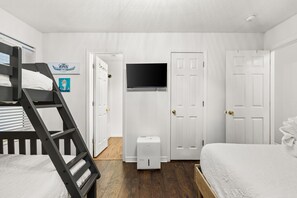 A bedroom with a bunk bed, a flat-screen TV mounted on a door, and a small bedside table.