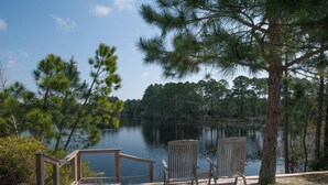 A lakeside deck with two wooden chairs and a wooden railing overlooking a calm lake surrounded by pine trees.