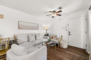A living room with a sofa, a coffee table, a lamp, and a ceiling fan.