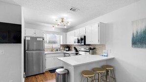 A modern kitchen with white cabinetry, stainless steel appliances, a central island with stools, and a ceiling light fixture.
