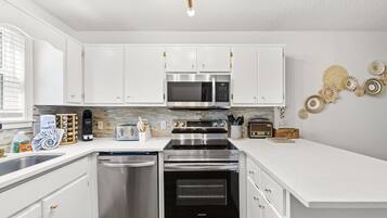 A modern kitchen with white cabinetry, stainless steel appliances, and a built-in microwave.