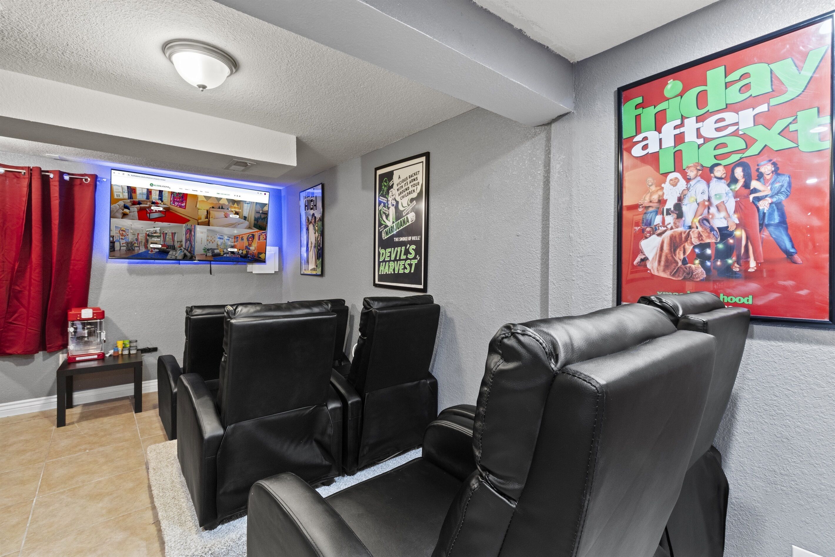 A home theater room with black leather recliners, a small table with a coffee maker, and a large poster on the wall.