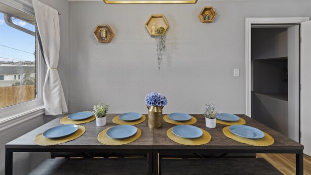 Une table à manger dressée avec de l’assiette bleue et des sets de table dorés, un vase rempli de fleurs bleues et des décorations murales hexagonales.