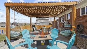 Un espace patio agrémenté d’une pergola, de sièges d’extérieur, d’un foyer et de fauteuils suspendus.