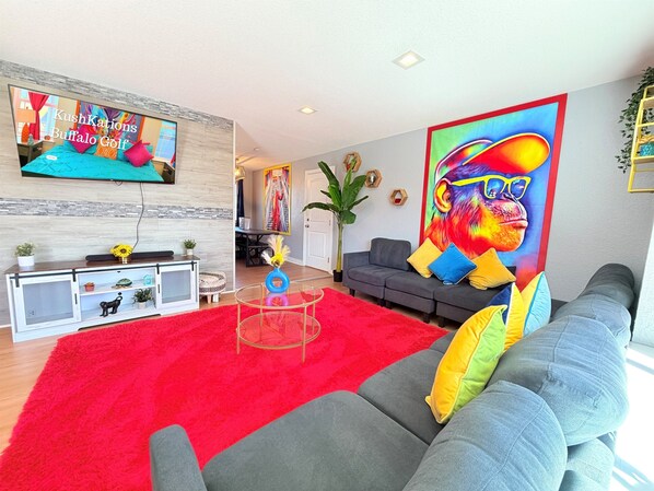Un salon moderne avec un canapé gris, une moquette rouge et un téléviseur fixé au mur.