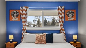 Une chambre avec un grand lit, deux tables de chevet, une fenêtre avec des rideaux et deux œuvres d’art murales.
