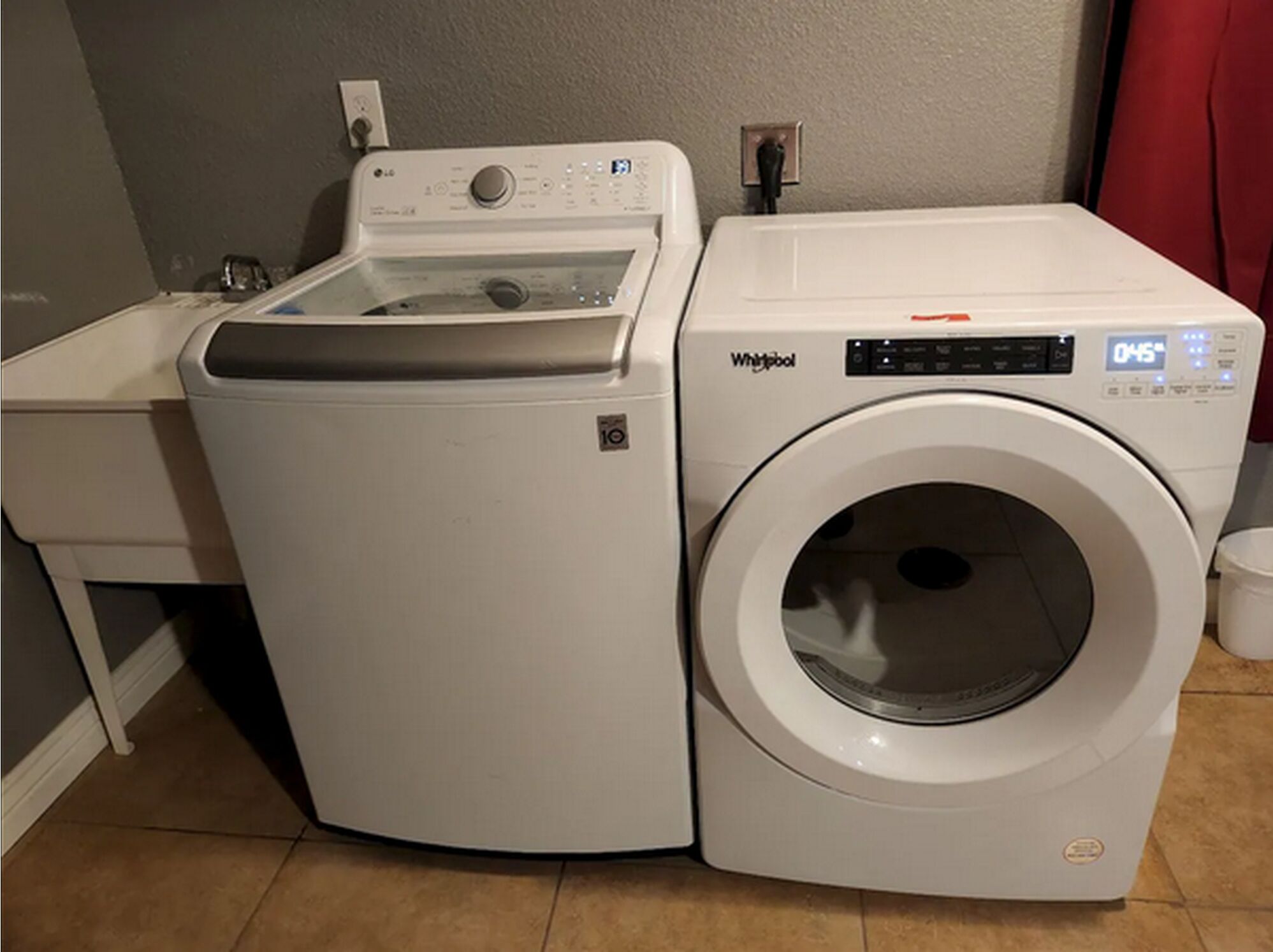 Een voorlader wasmachine en droger staan naast elkaar in een wasruimte met een betegelde vloer en een rood gordijn op de achtergrond.