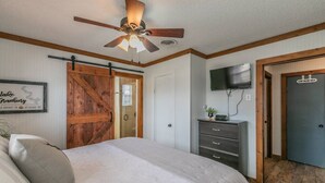 A bedroom with a bed, a ceiling fan, a wooden door, a dresser, and a TV mounted on the wall.
